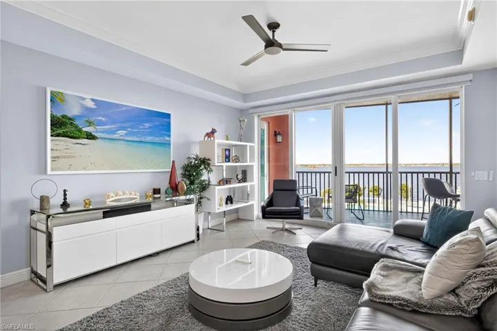 Living area with ornamental molding, light tile patterned floors, ceiling fan, and a raised ceiling