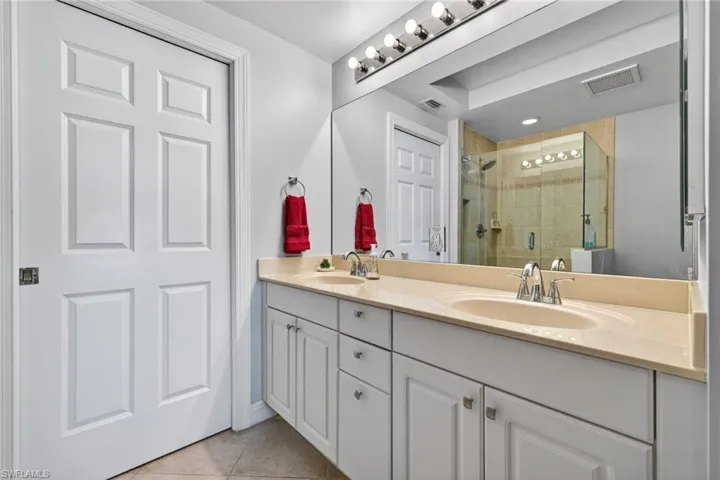 Full bath with double vanity, light tile patterned floors, and a shower stall