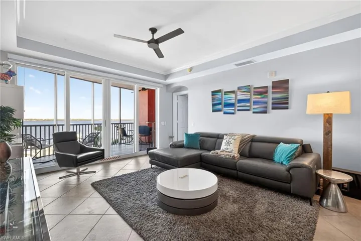 Living area featuring a raised ceiling, crown molding, a water view, arched walkways, and light tile patterned floors
