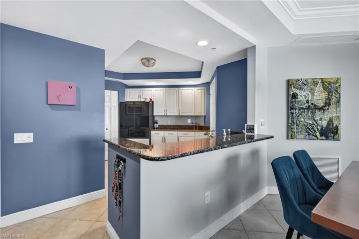 Kitchen featuring a raised ceiling, dark stone countertops, black refrigerator, light tile patterned floors, and recessed lighting