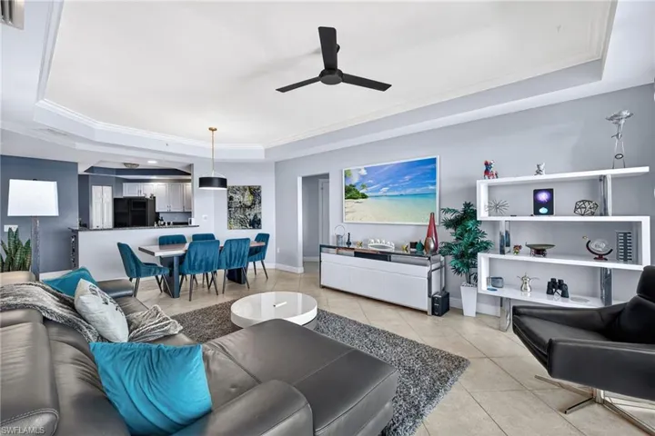 Living room with a tray ceiling, crown molding, a ceiling fan, and light tile patterned floors