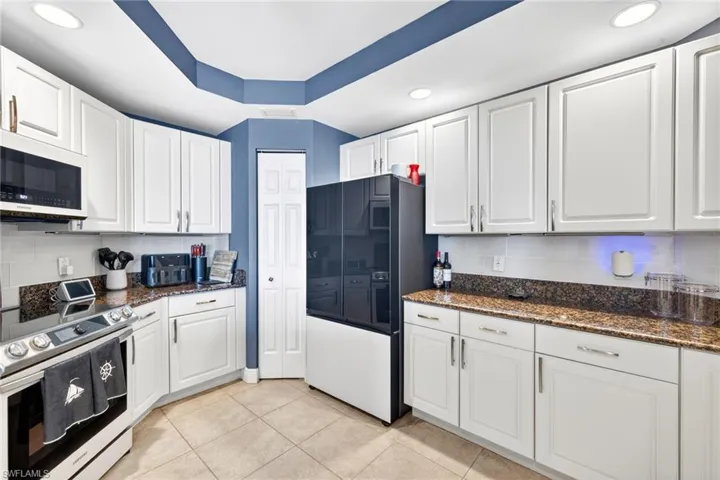 Kitchen featuring stainless steel electric stove, white cabinetry, freestanding refrigerator, dark stone countertops, and recessed lighting