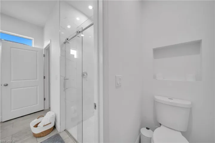 Contemporary bathroom featuring a frameless glass shower enclosure, recessed shower niche, and a wall-mounted niche above the toilet