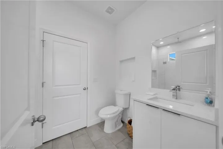 Modern bathroom featuring a single vanity with a white countertop and integrated sink, a large wall-mounted mirror, and sleek white cabinetry