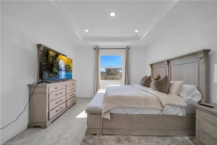 Spacious room featuring a tray ceiling with recessed lighting, light-toned wood-finish flooring, and a large window with drapes