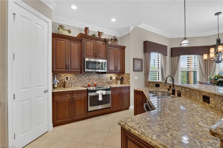 Kitchen featuring appliances with stainless steel finishes, decorative light fixtures, a chandelier, light stone counters, and ornamental molding