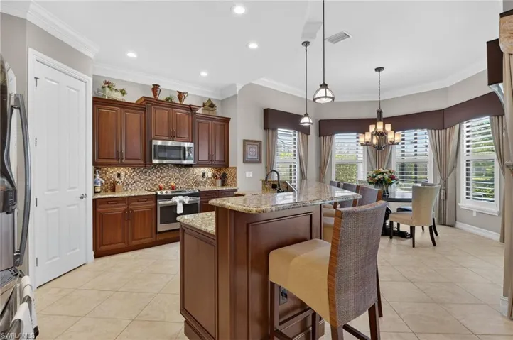 Kitchen featuring a breakfast bar area, decorative light fixtures, an island with sink, light stone countertops, and light tile patterned floors