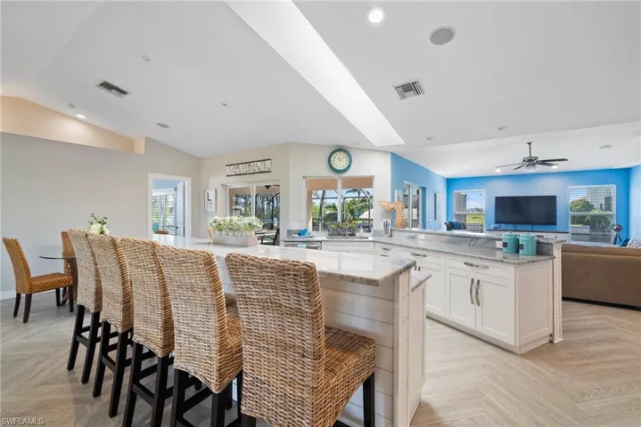 Kitchen with light parquet floors, white cabinetry, light stone countertops, and a kitchen bar