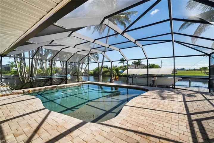 View of pool with a jacuzzi, a patio area, a water view, and glass enclosure