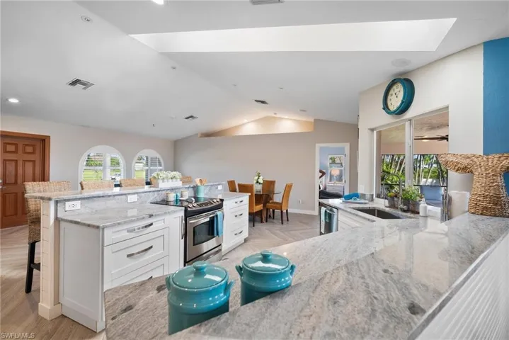 Kitchen featuring a breakfast bar, lofted ceiling with skylight, stainless steel appliances, light stone counters, and white cabinets