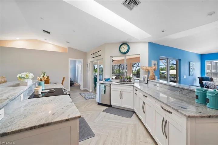 Kitchen with vaulted ceiling with skylight, white cabinetry, light parquet floors, stainless steel dishwasher, and light stone countertops
