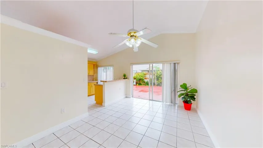 Empty room with vaulted ceiling, crown molding, light tile patterned floors, and ceiling fan