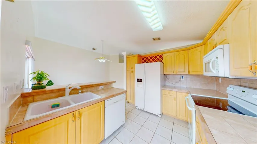 Kitchen with white appliances, tile counters, light brown cabinets, and crown molding