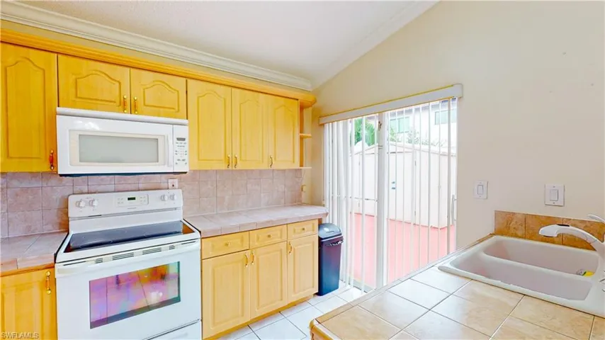 Kitchen featuring white appliances, crown molding, tile counters, light brown cabinets, and backsplash