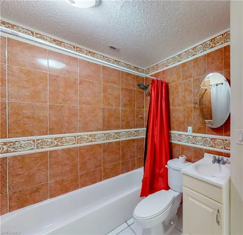 Full bathroom featuring a textured ceiling, shower / bath combo, vanity, tile patterned flooring, and tile walls