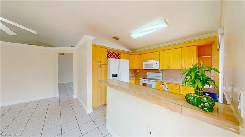Kitchen with tasteful backsplash, white appliances, vaulted ceiling, crown molding, and light tile patterned floors