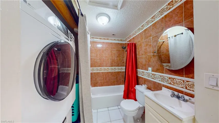Full bath with washer / clothes dryer, tile walls, a textured ceiling, vanity, and shower / bathtub combination with curtain
