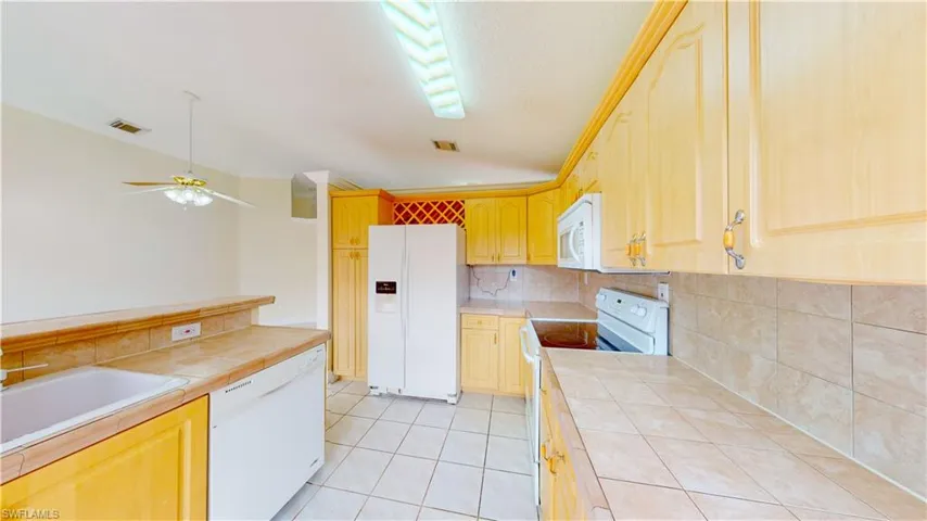 Kitchen with white appliances, crown molding, light brown cabinetry, decorative backsplash, and a ceiling fan