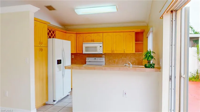 Kitchen featuring white appliances, light countertops, a peninsula, tasteful backsplash, and light tile patterned flooring