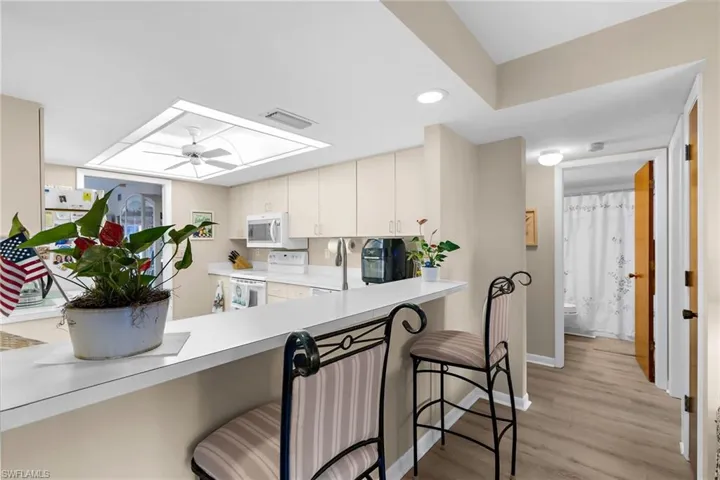 Kitchen featuring a breakfast bar area, light countertops, white appliances, light wood-style flooring, and a ceiling fan