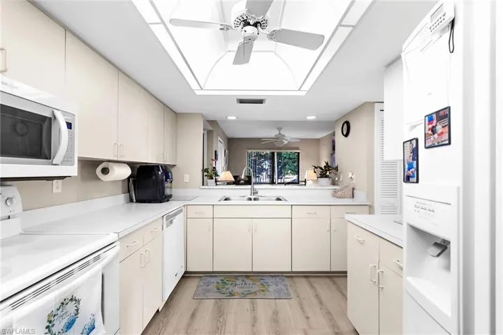 Kitchen with white appliances, a ceiling fan, light countertops, light wood-type flooring, and cream cabinets