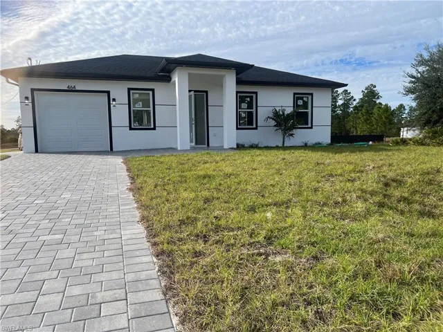 View of front of property with a front lawn, a garage, decorative driveway, stucco siding, and roof with shingles