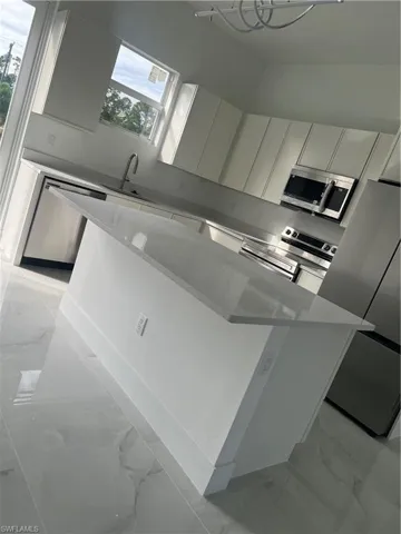 Kitchen featuring light marble finish flooring, a kitchen island, white cabinets, and refrigerator