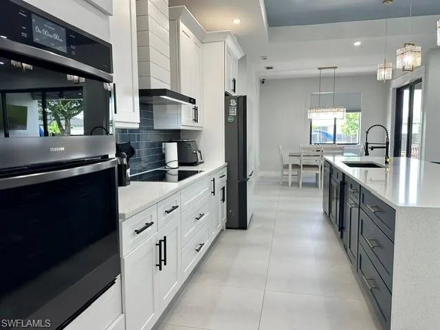 Gourmet kitchen featuring a built-in oven, contemporary flat-panel cabinetry, a large center island with an undermount sink, and durable tile flooring
