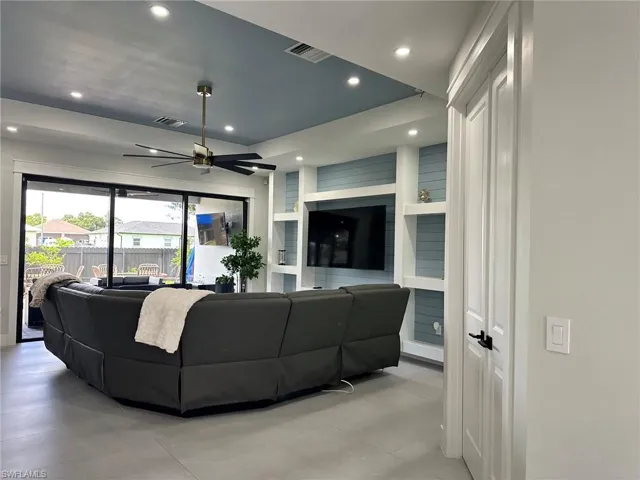 Recessed lighting throughout, modern ceiling fan, built-in entertainment center with shelving, large sliding glass doors, and tile flooring