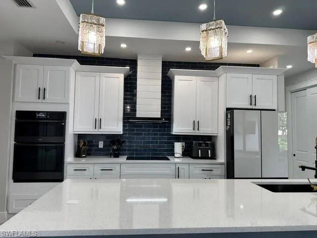 White shaker cabinetry with dark hardware, built-in double ovens, light-toned countertops, and a dark tile backsplash