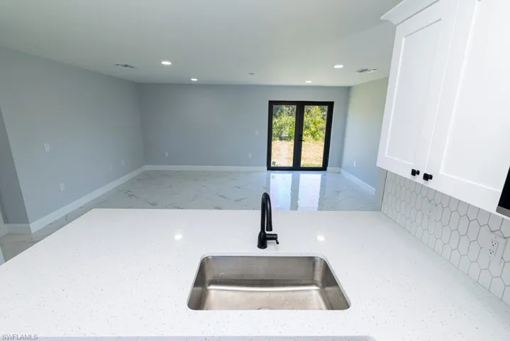 Kitchen with white cabinets, light stone countertops, sink, and french doors