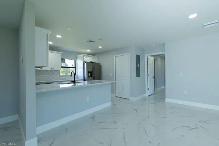 Kitchen featuring white cabinetry, sink, stainless steel refrigerator with ice dispenser, backsplash, and kitchen peninsula