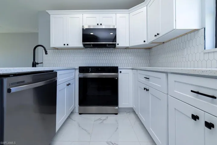 Kitchen with white cabinets, backsplash, light stone countertops, and stainless steel appliances