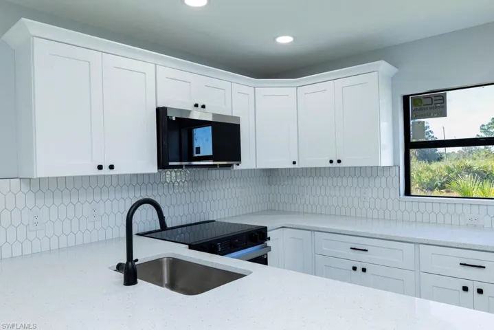 Kitchen featuring decorative backsplash, light stone countertops, sink, and white cabinets