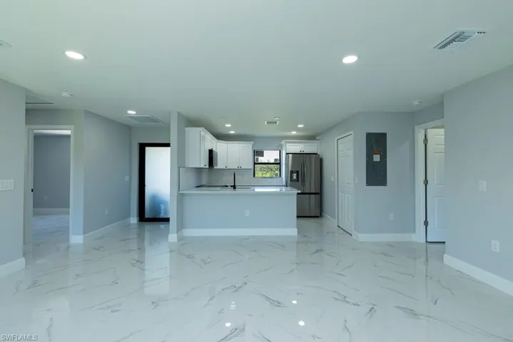 Kitchen featuring backsplash, electric panel, stainless steel refrigerator with ice dispenser, white cabinetry, and kitchen peninsula