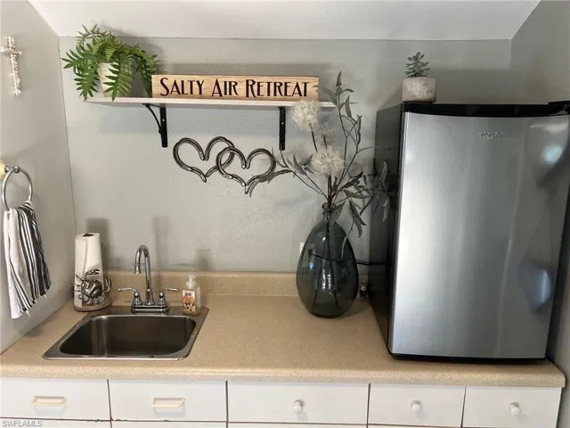 Kitchen featuring sink, white cabinetry, and stainless steel refrigerator