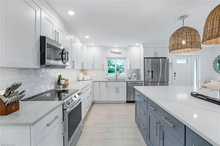 Kitchen with light stone counters, white cabinets, stainless steel appliances, and hanging light fixtures