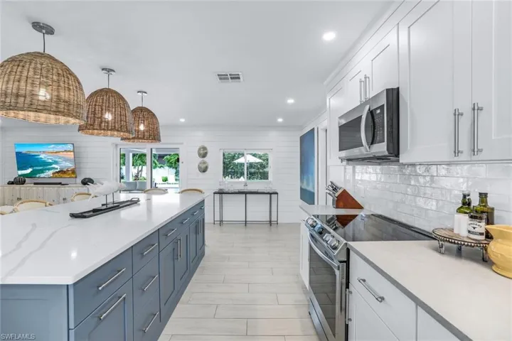 Kitchen with white cabinetry, hanging light fixtures, stainless steel appliances, backsplash, and blue cabinetry