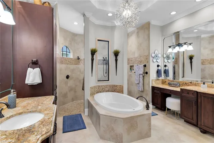 Full bath featuring a walk in shower, crown molding, two vanities, suspended lighting, and a garden tub