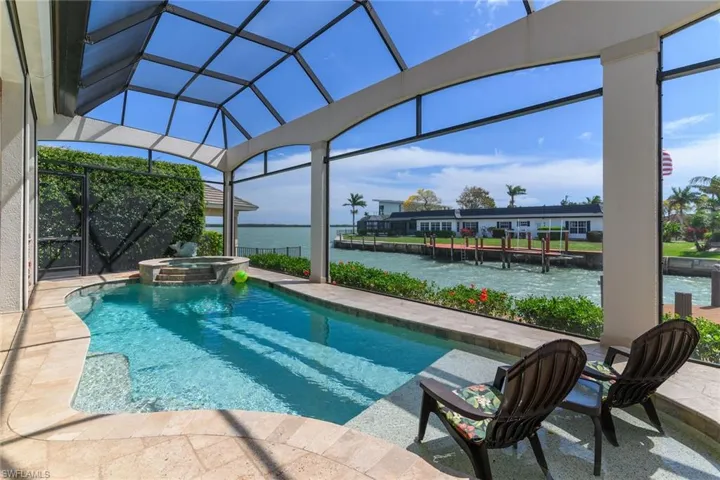 Integrated pool / hot tub featuring a sunroom, a patio, a water view, and glass enclosure