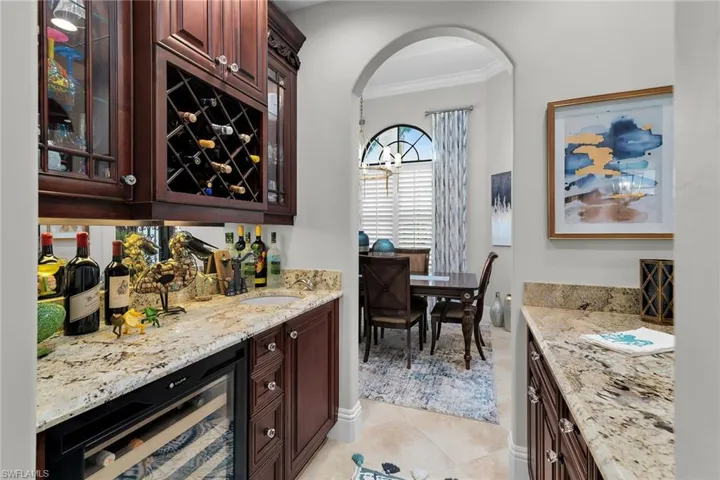 Indoor dry bar featuring dark wood finish cabinetry, beverage cooler, crown molding, light stone counters, and glass fronted cabinets