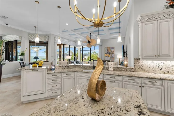 Kitchen with suspended lighting, coffered ceiling, white cabinets, light stone counters, and open floor plan