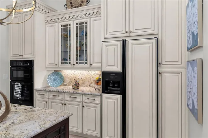 Two tone kitchen featuring paneled refrigerator, glass fronted cabinets, light stone countertops, and two tone cabinetry