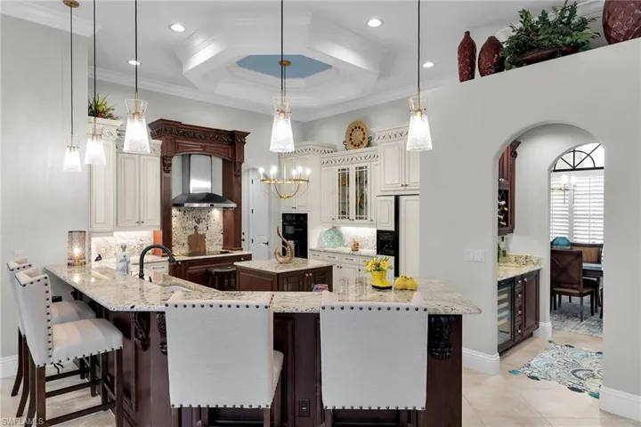 Kitchen with coffered ceiling, a kitchen bar, backsplash, dual tone cabinets, and light stone countertops