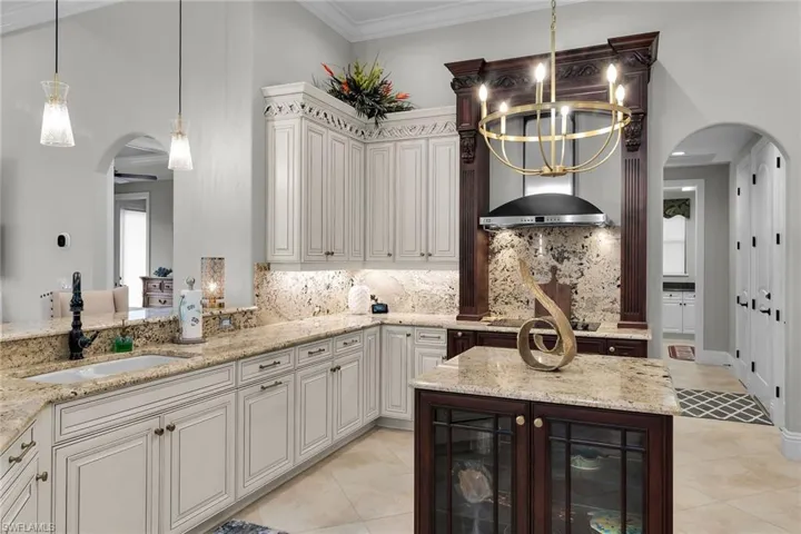 Dual tone kitchen featuring arched walkways, a center island, light stone counters, light tile patterned floors, and crown molding