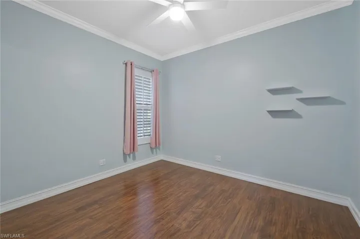 Empty room with baseboards, dark wood-style floors, ceiling fan, and crown molding