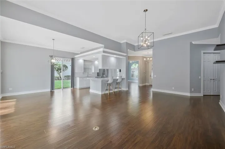 Unfurnished living room featuring an inviting chandelier, plenty of natural light, baseboards, and wood finished floors