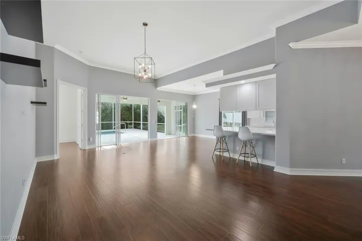 Unfurnished living room with a wealth of natural light, a notable chandelier, baseboards, and wood finished floors