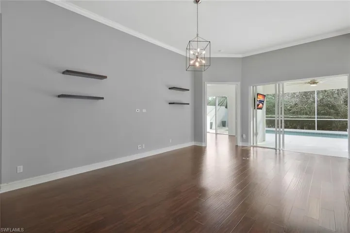 Unfurnished room featuring baseboards, ceiling fan with notable chandelier, wood finished floors, and ornamental molding