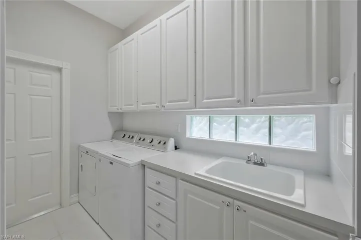 Laundry area with light tile patterned flooring, independent washer and dryer, cabinet space, and a sink